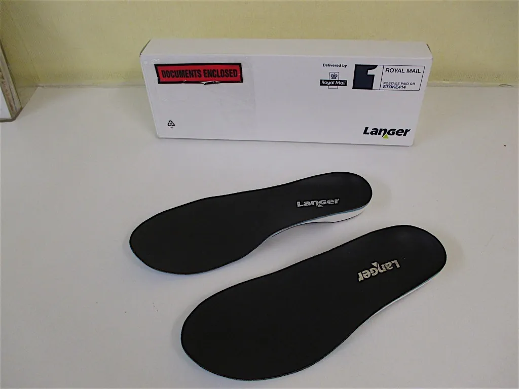 A pair of black Langer insoles in front of their delivery box